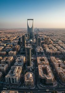 لماذا أصبحت الرياض مختبرًا مفتوحًا للعمارة العالمية؟
لم تعد الرياض مجرد عاصمة تتوسع عمرانيًا مع النمو السكاني والاقتصادي، بل أصبحت واحدة من أكثر المدن إثارة للاهتمام في المشهد المعماري العالمي. خلال السنوات الأخيرة، تحولت العاصمة السعودية إلى مساحة واسعة لاختبار أفكار جديدة في التصميم، والتخطيط الحضري، والاستدامة، والتكنولوجيا، وتجربة المستخدم.
وفي الوقت الذي تتسابق فيه المدن الكبرى حول العالم على بناء رموز معمارية جديدة، تبدو الرياض مختلفة في حجم التجربة وسرعتها وتنوعها. فالمشهد العمراني فيها لا يعتمد على مدرسة معمارية واحدة، وإنما يجمع بين العمارة المعاصرة، والتقنيات المستقبلية، والمفردات المستوحاة من البيئة السعودية، إلى جانب مشاريع ضخمة تعيد التفكير في علاقة المبنى بالمدينة.
من هنا ظهر مفهوم يمكن وصفه بـ العمارة العالمية في الرياض؛ حيث أصبحت المدينة مساحة يلتقي فيها المعماريون والمصممون والمطورون والخبرات الهندسية من أنحاء مختلفة من العالم لتقديم حلول جديدة لمستقبل المدن.
لكن لماذا أصبحت الرياض تحديدًا مختبرًا مفتوحًا للعمارة العالمية؟ وما الذي يجعل تجربتها مختلفة عن مجرد طفرة في البناء؟
الرياض من مدينة نامية إلى مختبر معماري مفتوح
المدن تتغير عادة بشكل تدريجي، ويحتاج التحول العمراني فيها إلى سنوات طويلة حتى تظهر نتائجه. إلا أن الرياض تشهد وتيرة مختلفة؛ فالمشاريع الكبرى، والاستثمارات الضخمة، والتوسع الحضري، والرؤية المستقبلية للمدينة، كلها تعمل في الوقت نفسه على إعادة تشكيل المشهد العمراني.
وهذا التحول لا يتعلق بعدد المباني الجديدة فقط، بل بطريقة التفكير في المدينة نفسها.
فالمشروع المعماري اليوم لا يُنظر إليه باعتباره مبنى منفصلًا عن محيطه، وإنما باعتباره جزءًا من منظومة أكبر تشمل الحركة، والخدمات، والمساحات العامة، والبيئة، والتقنية، وتجربة الإنسان.
لذلك يمكن النظر إلى الرياض باعتبارها مختبرًا مفتوحًا؛ لأن الكثير من الأفكار التي يتم اختبارها فيها تتجاوز حدود المبنى الواحد لتؤثر في شكل الأحياء والمناطق الحضرية ومستقبل المدينة.
المشاريع الكبرى تفتح الباب أمام أفكار أكثر جرأة
أحد أهم أسباب ازدهار العمارة العالمية في الرياض هو ظهور مشاريع ضخمة تتطلب حلولًا غير تقليدية.
عندما يكون المشروع صغيرًا، يمكن الاعتماد على حلول تصميمية معروفة ومجربة. أما عندما نتحدث عن مناطق حضرية ضخمة، ومراكز أعمال، ومشاريع ثقافية وترفيهية، ومجمعات متعددة الاستخدامات، فإن حجم التحديات يصبح أكبر بكثير.
كيف يمكن تصميم مبنى قادر على استيعاب أعداد كبيرة من المستخدمين؟
كيف يمكن تقليل استهلاك الطاقة في بيئة مناخية حارة؟
كيف يمكن توفير مساحات عامة مريحة وجذابة؟
كيف يمكن دمج وسائل النقل والخدمات والتكنولوجيا داخل المشروع؟
هذه الأسئلة تدفع المعماريين إلى تجاوز الحلول التقليدية والبحث عن أفكار أكثر ابتكارًا.
ولهذا أصبحت المشاريع الكبرى في الرياض فرصة حقيقية لتجربة أشكال جديدة من العمارة والتخطيط الحضري.
عندما تلتقي العمارة العالمية بالهوية السعودية
قد يبدو الانفتاح على الخبرات العالمية وكأنه طريق يؤدي إلى تشابه المدن، لكن تجربة الرياض تحمل تحديًا مختلفًا: كيف يمكن الاستفادة من الخبرات العالمية دون فقدان الهوية المحلية؟
الإجابة بدأت تظهر في عدد من الاتجاهات المعمارية التي تحاول إعادة تفسير العناصر السعودية بأسلوب معاصر.
فالهوية المعمارية لا تعني بالضرورة إعادة إنتاج المباني التراثية كما هي، وإنما يمكن التعبير عنها من خلال النسب، والخامات، والظلال، والفراغات، والأنماط الهندسية، وطريقة التعامل مع المناخ.
على سبيل المثال، يمكن أن تتحول فكرة الفناء الداخلي التقليدي إلى مساحة معاصرة تجمع بين الخصوصية والتهوية والتواصل الاجتماعي.
كما يمكن إعادة تفسير الأنماط الهندسية المحلية في الواجهات الحديثة، أو استخدام خامات وألوان مستوحاة من البيئة المحيطة بطريقة أكثر بساطة.
وهنا تصبح العمارة العالمية في الرياض عملية تبادل وليست استيرادًا؛ فالخبرة العالمية تدخل إلى السياق السعودي، ثم يعاد تشكيلها وفق احتياجات المكان وثقافته ومناخه.
المناخ السعودي يصبح جزءًا من فكرة التصميم
لا يمكن الحديث عن مستقبل العمارة في الرياض دون الحديث عن المناخ.
فالحرارة المرتفعة والإشعاع الشمسي يمثلان تحديات حقيقية أمام المصممين، لكنهما في الوقت نفسه يمثلان فرصة لتطوير حلول معمارية أكثر ذكاءً.
أصبحت الواجهة المعمارية الحديثة مطالبة بأداء وظائف متعددة في الوقت نفسه. فهي ليست مجرد عنصر جمالي، وإنما يمكن أن تساهم في تقليل اكتساب الحرارة، والتحكم في دخول الضوء، وتحسين كفاءة الطاقة.
ولهذا تظهر أهمية عناصر مثل التظليل، والزجاج عالي الأداء، والعزل الحراري، والواجهات المتجاوبة، وتوجيه المبنى وفق حركة الشمس.
وبذلك يتحول المناخ من عائق إلى محفز للابتكار.
فالعمارة الناجحة في الرياض ليست بالضرورة الأكثر غرابة في شكلها، وإنما الأكثر قدرة على تحقيق التوازن بين الجمال والأداء.
التكنولوجيا تعيد رسم حدود الممكن
من أهم العوامل التي جعلت الرياض بيئة مناسبة للتجارب المعمارية تطور التكنولوجيا.
أدوات التصميم الرقمي أصبحت تسمح للمعماريين باختبار أشكال معقدة، وتحليل أداء المباني، ومحاكاة حركة الشمس والرياح، ودراسة حركة المستخدمين قبل بدء التنفيذ.
كما ساهمت تقنيات التصنيع الحديثة في جعل بعض الأشكال المعمارية التي كانت صعبة التنفيذ أكثر قابلية للتحقيق.
وهذا يعني أن العلاقة بين المعماري والمهندس والمقاول أصبحت أكثر تكاملًا من أي وقت مضى.
فالتصميم لا ينتهي عند إنتاج النموذج ثلاثي الأبعاد، بل يستمر من خلال مراحل التحليل، والتطوير، والتنسيق، والتنفيذ.
وفي مدينة تشهد هذا الحجم من المشاريع، تصبح التكنولوجيا أداة أساسية لتقليل الأخطاء وتحسين الأداء وتحويل الأفكار الجريئة إلى مبانٍ قابلة للتنفيذ.
الذكاء الاصطناعي ومستقبل التصميم المعماري
من المتوقع أن يكون الذكاء الاصطناعي أحد الأدوات التي ستؤثر بصورة أكبر في مستقبل العمارة العالمية في الرياض.
فالذكاء الاصطناعي يمكن أن يساعد في تحليل كميات ضخمة من البيانات، واقتراح بدائل تصميمية، ودراسة كفاءة الطاقة، وتحليل حركة المستخدمين، والمساعدة في اتخاذ قرارات مبكرة خلال مراحل التصميم.
لكن أهمية هذه الأدوات لا تكمن في قدرتها على إنتاج صور جذابة فقط.
القيمة الحقيقية تظهر عندما يتم استخدام التكنولوجيا لتحسين القرار المعماري نفسه.
فالمبنى المستقبلي لا يحتاج فقط إلى شكل مميز، بل يحتاج إلى أن يكون مناسبًا للمناخ، فعالًا في استهلاك الطاقة، مريحًا للمستخدم، وقابلًا للتنفيذ.
وهنا تصبح التكنولوجيا وسيلة للوصول إلى عمارة أكثر ذكاءً، وليس مجرد وسيلة لصناعة أشكال مستقبلية.
الرياض تجمع مدارس معمارية مختلفة في مشهد واحد
من المثير في المشهد العمراني للرياض أنك قد تجد داخل المدينة نفسها اتجاهات معمارية متعددة.
هناك مشاريع تعتمد على الخطوط الهندسية الواضحة، وأخرى تميل إلى الأشكال العضوية، ومشاريع تستلهم التراث، وأخرى تتجه بقوة نحو المستقبل.
هذا التنوع يجعل المدينة أشبه بمعرض معماري مفتوح.
لكن الأهم أن هذه المشاريع لا تتنافس فقط على الشكل، بل تقدم تجارب مختلفة حول كيفية استخدام المبنى والمدينة.
بعض المشاريع يركز على العمل والأعمال، وأخرى على الثقافة والترفيه، وأخرى على المساحات العامة، بينما تجمع مشاريع أخرى بين أكثر من وظيفة داخل منطقة واحدة.
وهذا التنوع يخلق بيئة تسمح بمقارنة الحلول المختلفة واكتشاف ما يناسب طبيعة الرياض بشكل أفضل.
من المبنى إلى التجربة
العمارة الحديثة لم تعد تتعامل مع المبنى باعتباره مجموعة من الجدران والأسقف والواجهات.
اليوم أصبحت تجربة المستخدم جزءًا أساسيًا من التصميم.
كيف يصل الشخص إلى المبنى؟
كيف يتحرك داخله؟
هل يجد أماكن للراحة؟
هل يشعر بالارتباط بالمساحة؟
هل المبنى واضح وسهل الاستخدام؟
هل المساحات الخارجية مريحة خلال الظروف المناخية المختلفة؟
هذه الأسئلة أصبحت أكثر أهمية مع تطور المشاريع متعددة الاستخدامات.
ومن هنا يظهر تحول مهم في الرياض: التركيز لا يكون فقط على إنشاء مبانٍ مميزة بصريًا، وإنما على بناء أماكن يمكن للناس استخدامها والاستمتاع بها.
الاستدامة ليست رفاهية
مع توسع الرياض وارتفاع حجم النشاط العمراني، أصبحت الاستدامة عنصرًا أساسيًا في مستقبل التصميم والبناء.
والاستدامة في السياق السعودي لا تعني فقط إضافة ألواح شمسية أو زراعة بعض المساحات الخضراء.
إنها تبدأ من القرار التصميمي الأول.
اختيار اتجاه المبنى، حجم الفتحات، نوع الواجهة، المواد المستخدمة، أنظمة التكييف، إدارة المياه، الإضاءة الطبيعية، وإعادة استخدام الموارد؛ كلها قرارات تؤثر في أداء المبنى طوال دورة حياته.
لذلك فإن مستقبل العمارة في الرياض يعتمد بدرجة كبيرة على القدرة على إنتاج مبانٍ تجمع بين التصميم الجذاب والكفاءة التشغيلية.
وهنا يمكن أن تتحول المدينة إلى نموذج مهم لدراسة كيفية تطوير عمارة مستدامة في البيئات الحارة.
الخامات تحكي جزءًا من قصة المكان
الخامات المعمارية تلعب دورًا مهمًا في تشكيل هوية المبنى.
فالخرسانة، والحجر، والزجاج، والمعدن، والخشب، وغيرها من المواد يمكن أن تعطي المبنى شخصيته الخاصة.
وفي الرياض، يزداد الاهتمام باستخدام الخامات بطريقة تعكس البيئة المحلية دون الوقوع في التقليد المباشر للعمارة التراثية.
يمكن أن يكون المبنى معاصرًا بالكامل، ومع ذلك يحمل إحساسًا بالمكان من خلال الملمس واللون والظل ونسب الكتل.
وهذا يفتح الباب أمام مفهوم أكثر نضجًا للهوية المعمارية: هوية لا تعتمد على الزخرفة فقط، وإنما تظهر في تفاصيل التصميم والأداء والمواد.
هل الرياض تصنع لغة معمارية جديدة؟
ربما يكون هذا هو السؤال الأكثر أهمية.
وجود شركات ومكاتب تصميم عالمية في الرياض لا يعني تلقائيًا ظهور مدرسة معمارية سعودية.
لكن اجتماع عدة عوامل في الوقت نفسه قد يساعد على ظهور لغة جديدة:
خبرات عالمية + بيئة محلية مختلفة + مشاريع ضخمة + تكنولوجيا متقدمة + هوية ثقافية قوية.
عندما تجتمع هذه العناصر، يصبح من الممكن إنتاج عمارة لا تنتمي بالكامل إلى النماذج الغربية ولا تعيد إنتاج التراث المحلي كما هو، وإنما تقدم صيغة جديدة بين الاثنين.
وقد تكون هذه إحدى أهم نتائج التحول العمراني الذي تشهده الرياض.
الرياض كمدينة تختبر مستقبلها بنفسها
الميزة الأهم في تجربة الرياض أنها لا تنتظر حتى تصبح أفكار المستقبل جاهزة في مكان آخر ثم تبدأ في تطبيقها.
المدينة نفسها أصبحت مساحة لتجربة هذه الأفكار.
وهذا يجعل كل مشروع جديد بمثابة سؤال مفتوح:
هل يستطيع هذا التصميم تحسين تجربة المستخدم؟
هل يمكن تقليل استهلاك الطاقة؟
هل يمكن دمج التقنية دون التأثير على الجانب الإنساني؟
هل يمكن تحقيق هوية محلية داخل تصميم عالمي؟
هل يمكن بناء مدينة أكثر قابلية للمشي والتفاعل؟
الإجابة لا تأتي من التصميم وحده، وإنما من التجربة الفعلية بعد التنفيذ.
وهذا هو جوهر فكرة "المختبر المفتوح": أن المدينة نفسها تصبح مساحة للتجربة والتعلم والتطوير.
ما الذي يمكن أن تتعلمه المدن الأخرى من الرياض؟
تجربة الرياض لا تهم السعودية فقط.
فالعديد من المدن حول العالم تواجه تحديات مشابهة: النمو السكاني، ارتفاع درجات الحرارة، الحاجة إلى الاستدامة، تطوير النقل، وتحسين جودة الحياة.
لكن خصوصية الرياض تكمن في أنها تختبر هذه التحديات ضمن مرحلة تحول عمراني سريعة للغاية.
وإذا نجحت بعض الحلول التي يتم تطويرها اليوم، فقد تصبح قابلة للتطبيق في مدن أخرى ذات ظروف مناخية أو عمرانية مشابهة.
وهنا تتحول الرياض من متلقٍ للخبرة المعمارية إلى مصدر محتمل للمعرفة والخبرة.
بين الجرأة والهوية… أين يكمن مستقبل الرياض؟
قد يكون التحدي الأكبر أمام العمارة في الرياض هو تحقيق التوازن.
الجرأة مهمة، لكنها وحدها لا تكفي.
والتكنولوجيا مهمة، لكنها لا تصنع هوية.
والهوية مهمة، لكنها لا تعني العودة إلى الماضي.
والاستدامة ضرورية، لكنها يجب أن تكون جزءًا من التصميم وليس مجرد إضافة لاحقة.
العمارة الناجحة هي التي تجمع هذه العناصر داخل فكرة واحدة متماسكة.
مبنى يمكن أن يكون عالميًا دون أن يفقد علاقته بمكانه، ومعاصرًا دون أن يصبح منفصلًا عن ثقافته، ومستدامًا دون أن يفقد جماله.
وهذا بالضبط ما يجعل تجربة الرياض جديرة بالمتابعة.
الخلاصة: الرياض لا تبني مباني فقط… بل تختبر مستقبل العمارة
أصبحت الرياض مختبرًا مفتوحًا للعمارة العالمية لأنها تجمع مجموعة نادرة من العوامل في وقت واحد: مشاريع ضخمة، استثمارات كبيرة، انفتاح على الخبرات العالمية، تطور تقني، تحديات مناخية واضحة، واهتمام متزايد ببناء هوية سعودية معاصرة.
لكن القيمة الحقيقية لهذه التجربة لا تكمن في عدد الأبراج أو حجم المشاريع.
القيمة تكمن في الأسئلة التي تطرحها هذه المشاريع حول مستقبل المدينة والإنسان والعمارة.
كيف يمكن أن تبدو مدينة المستقبل في بيئة صحراوية؟
كيف يمكن أن تتعايش الهوية المحلية مع التصميم العالمي؟
كيف يمكن للتكنولوجيا أن تجعل المباني أكثر كفاءة؟
وكيف يمكن أن تتحول العمارة من مجرد شكل جميل إلى تجربة متكاملة؟
ربما لهذا السبب تحديدًا أصبحت العمارة العالمية في الرياض أكثر من مجرد اتجاه معماري.
إنها تجربة مستمرة لإعادة تعريف ما يمكن أن تكون عليه المدينة السعودية الحديثة.
والأهم أن التجربة لم تنتهِ بعد.
فالرياض ما زالت تبني، وتجرب، وتتعلم، وتعيد صياغة نفسها.
وربما بعد سنوات لن يكون السؤال: لماذا أصبحت الرياض مختبرًا مفتوحًا للعمارة العالمية؟
بل سيكون السؤال الأكثر إثارة:
ما الذي ستتعلمه بقية مدن العالم من الرياض؟